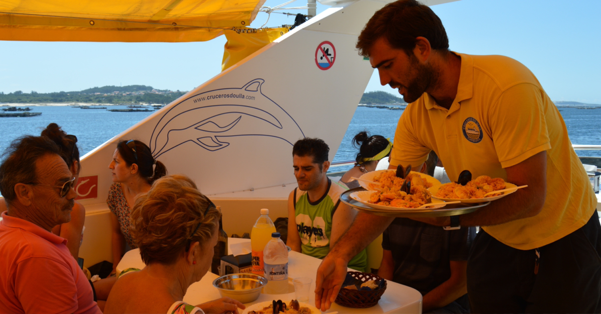 Pasajeros comiendo a bordo del barco restaurante marinero fondeado cerca de la playa de As Pipas