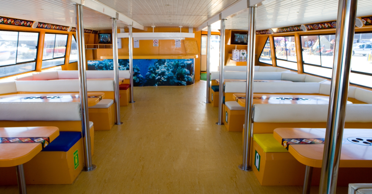 Comedor interior del catamarán Fly Delfín, amplio y luminoso, con mesas junto a las ventanas.