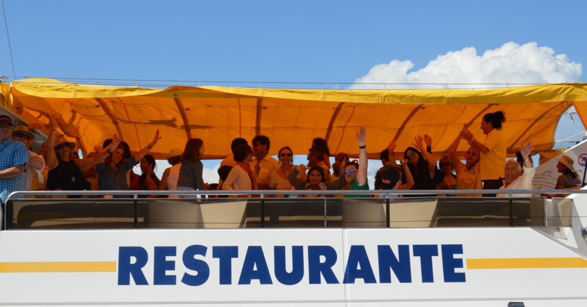 Cubierta trasera del barco restaurante con toldo amarillo y pasajeros disfrutando del regreso al puerto