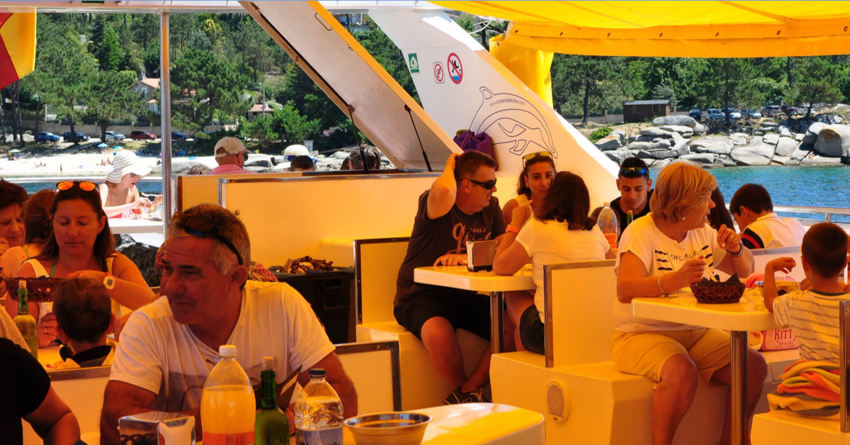 Pasajeros comiendo a bordo del barco restaurante marinero fondeado cerca de la playa de As Pipas
