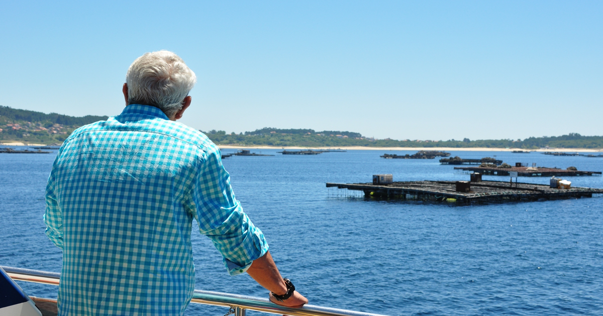 Un pasajero disfruta el paisaje desde la cubierta del barco. El fly Delfín Restaurante navegando cerca de las bateas en O Grove con las playas al fondo